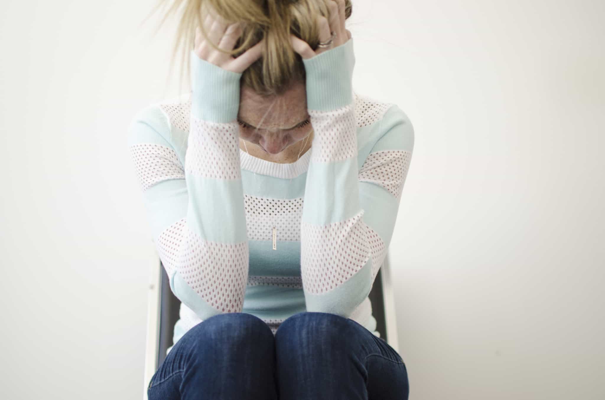 mulher jovem sentada com as mãos na cabeça preocupada