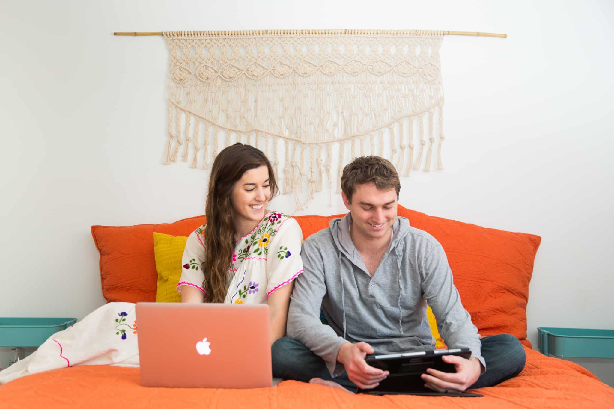 casal sentado em cima da cama com portatil e tablet