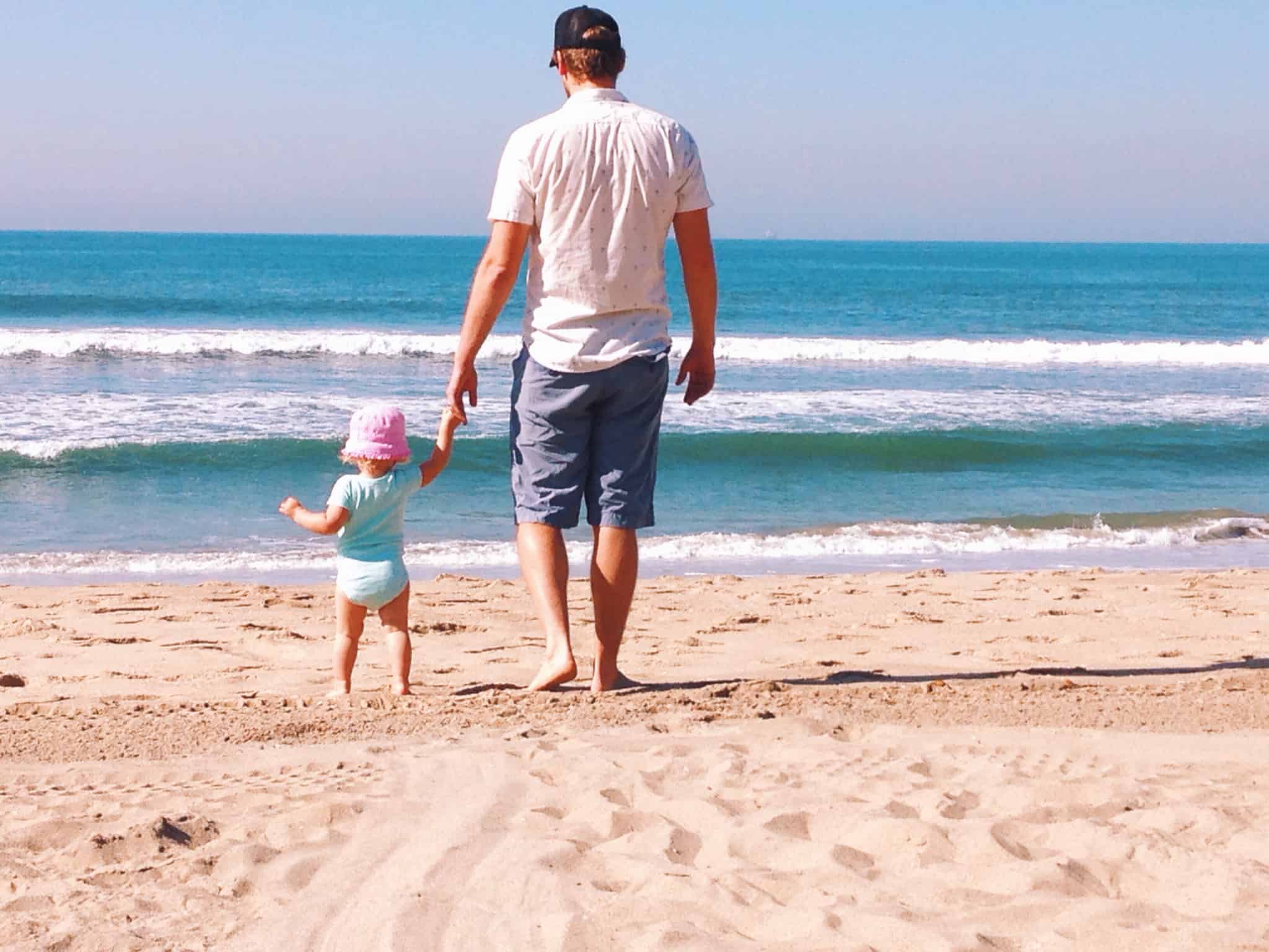 pai a passear o filho bebé na praia