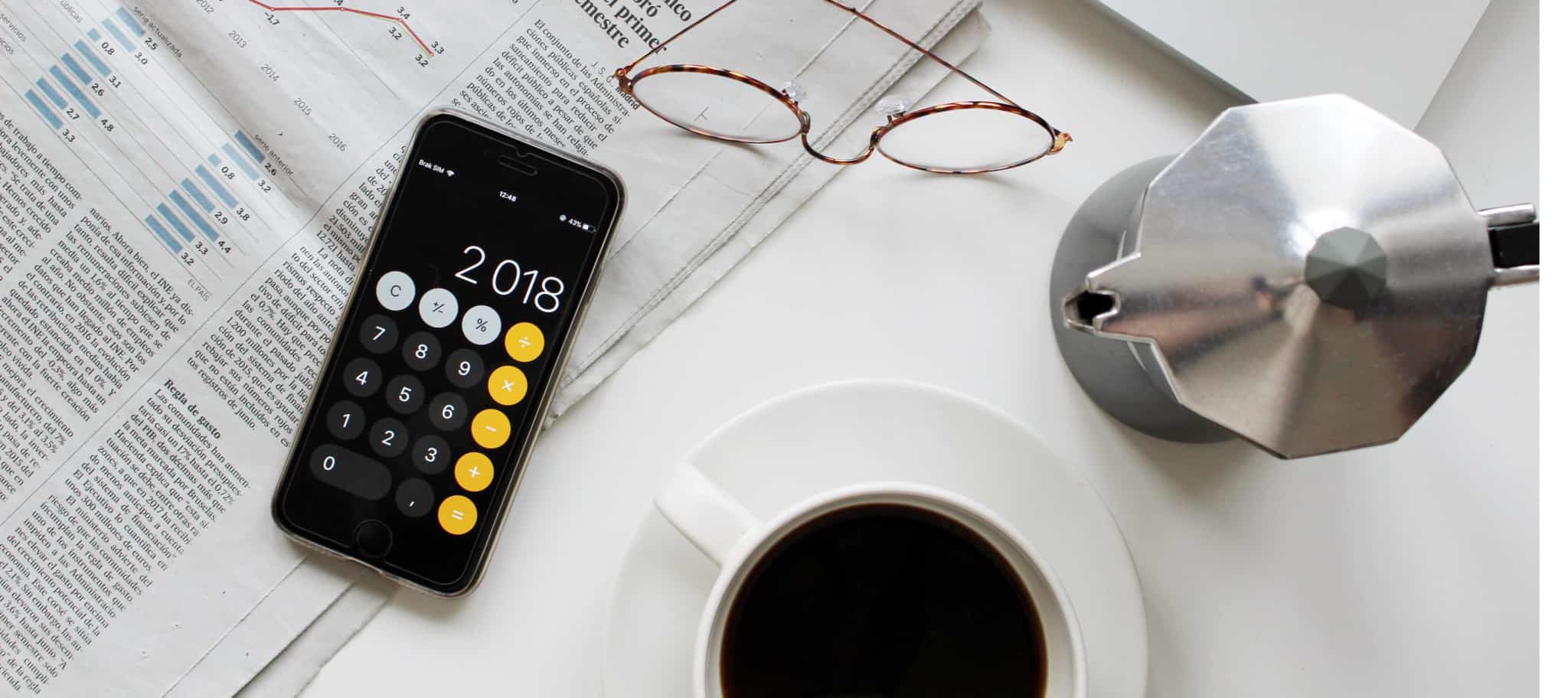 jornais abertos com calculadora em cima e chãvens de café