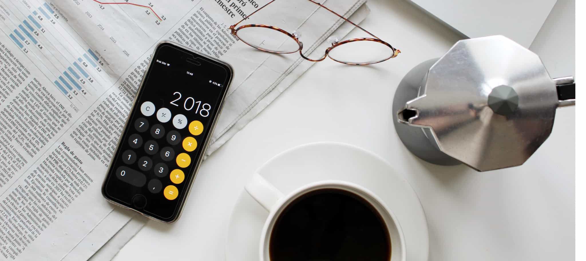 jornais abertos com calculadora em cima e chãvens de café