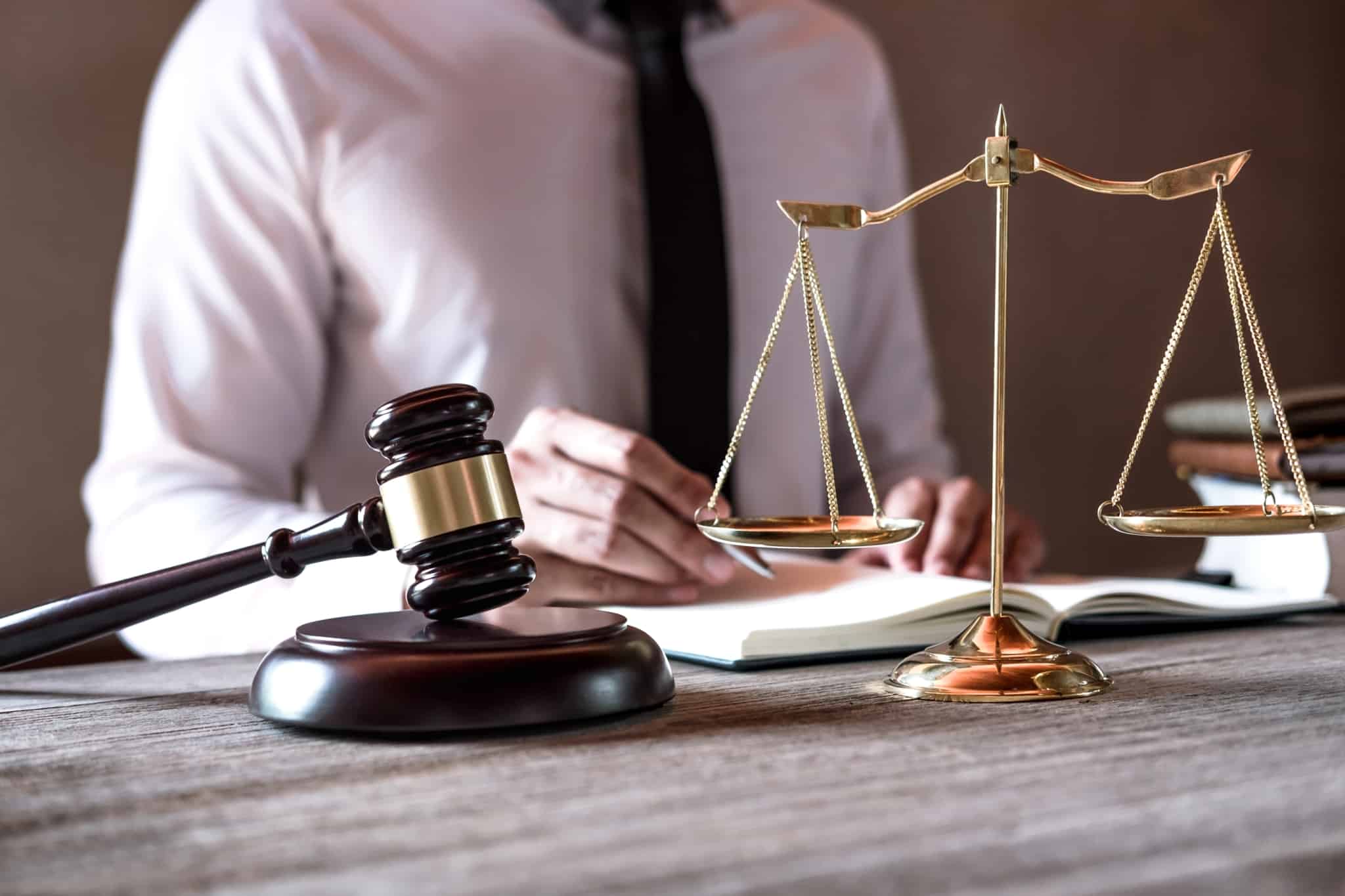 Homem a trabalhar numa mesa com uma balança e um martelo, símbolos de justiça