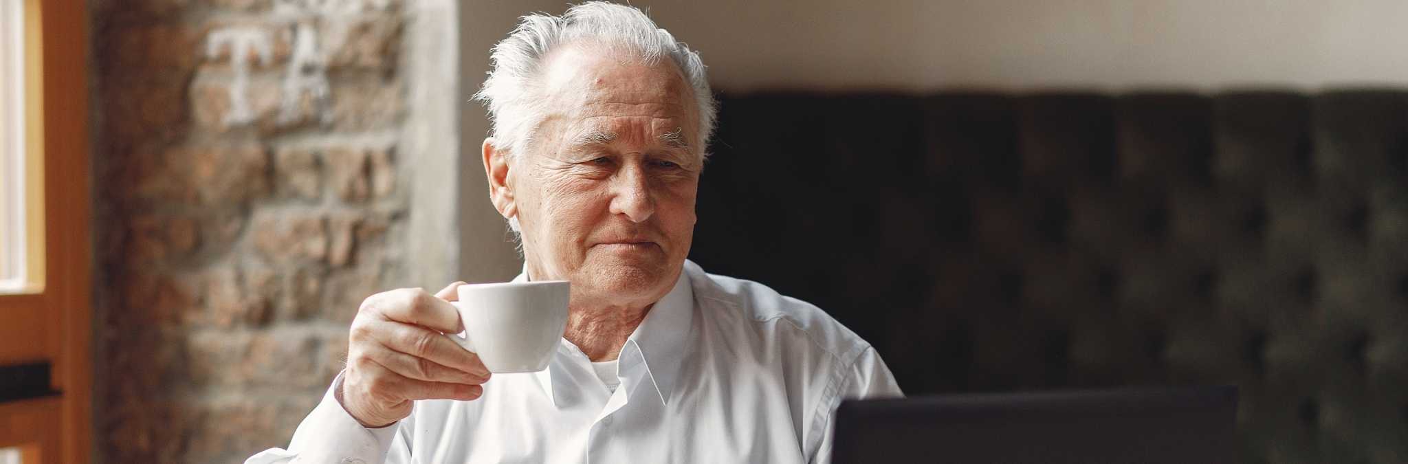 idoso a tomar café junto a computador