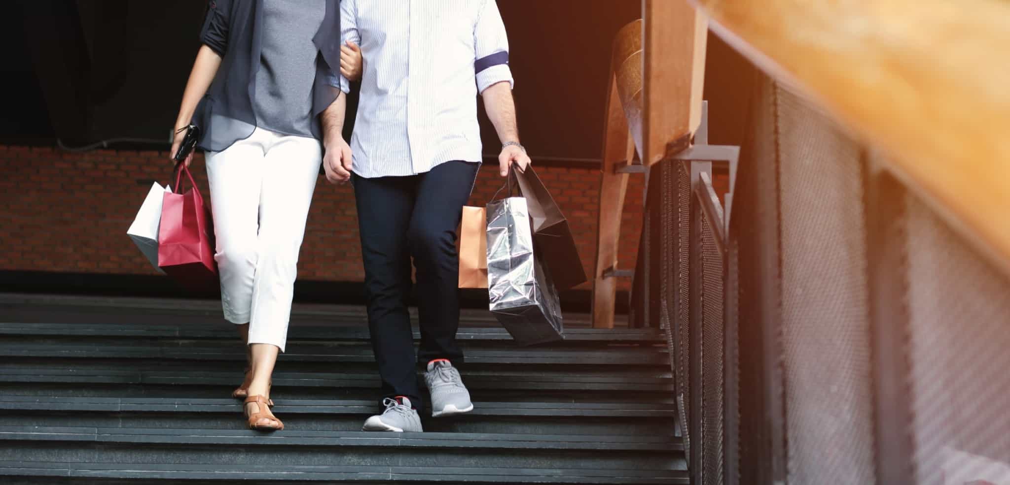 Um casal desce uma escadas com sacos de compras nas mãos