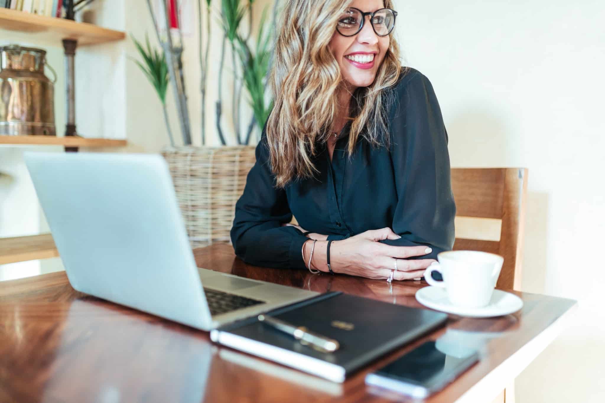 Mulher com ar feliz a trabalhar junto de um computador portátil e uma chávena de café