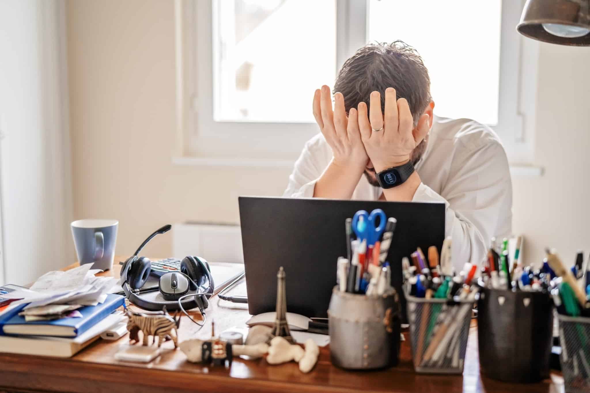 homem sentado em frente ao computador e de mãos na cara, num sinal de cansaço e frustração
