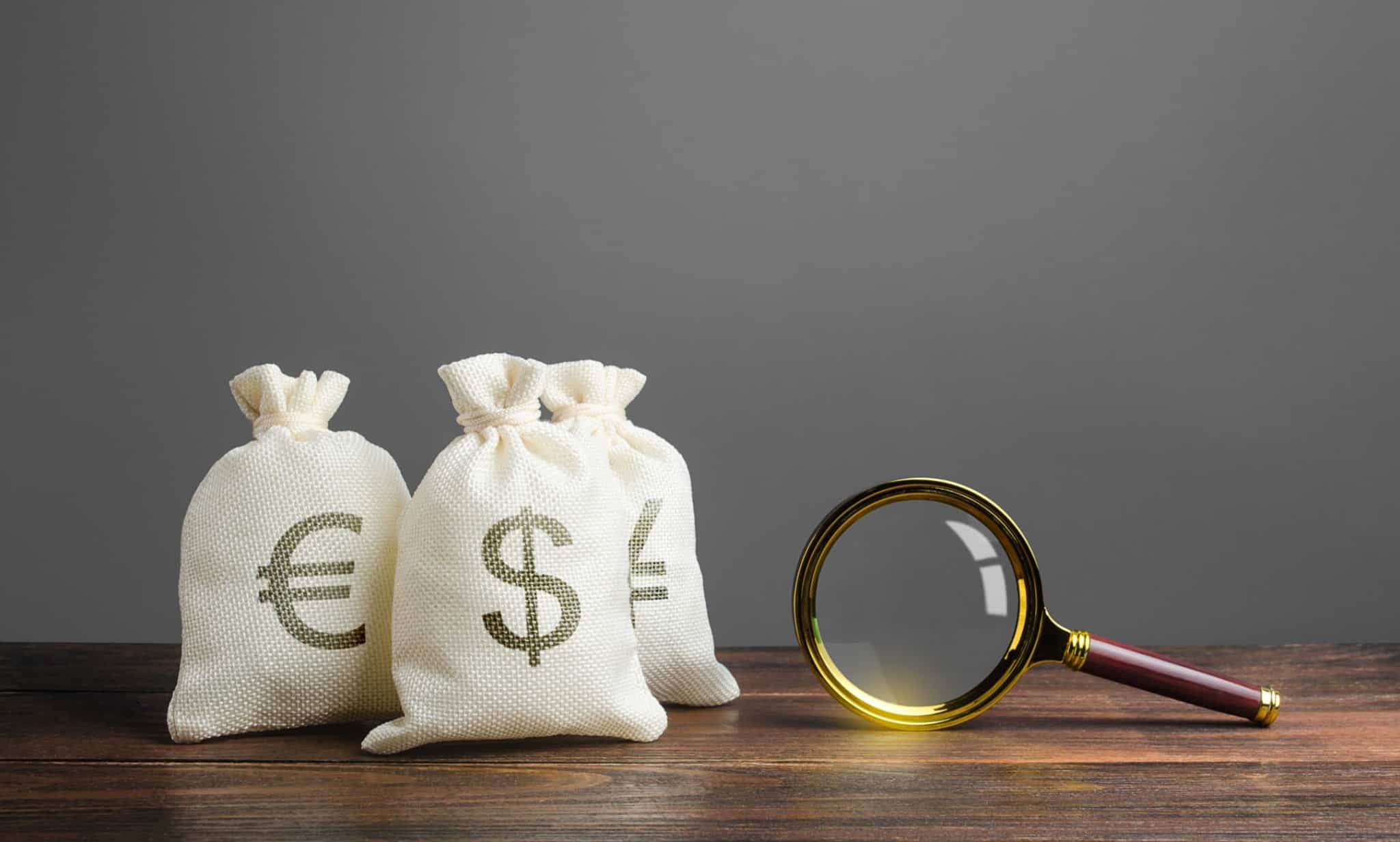 Sacos de serapilheira com símbolos de euro e dólar estampados e ao seu lado uma lupa