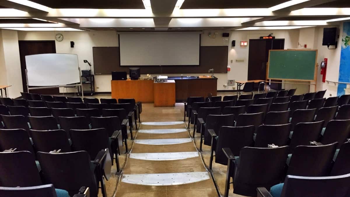 Sala de aula universidade com cadeiras, mesa professor e quadro