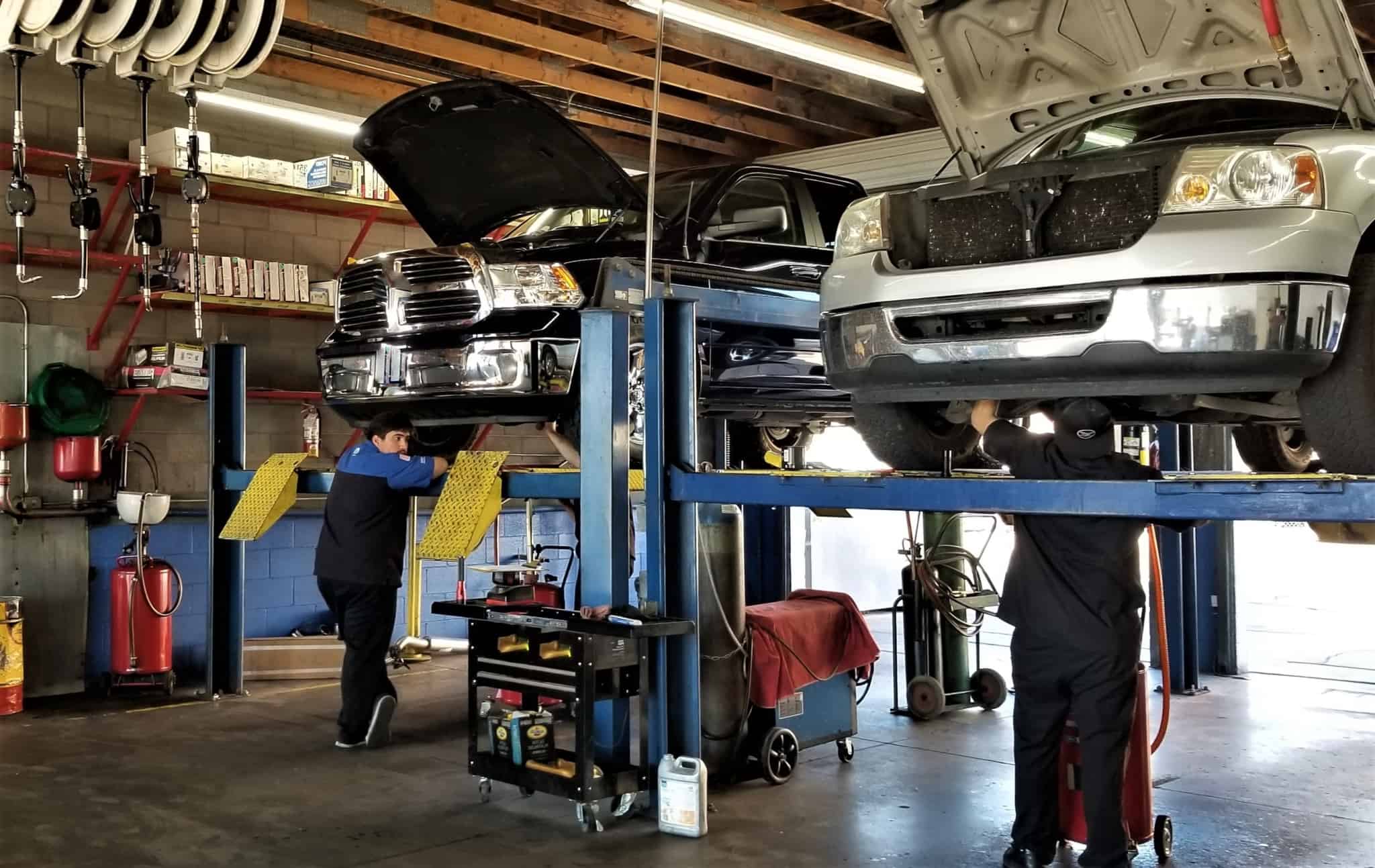 oficina de carros com dois automóveis a serem analisados por mecânicos. A manutenção pode reduzir as despesas com o carro