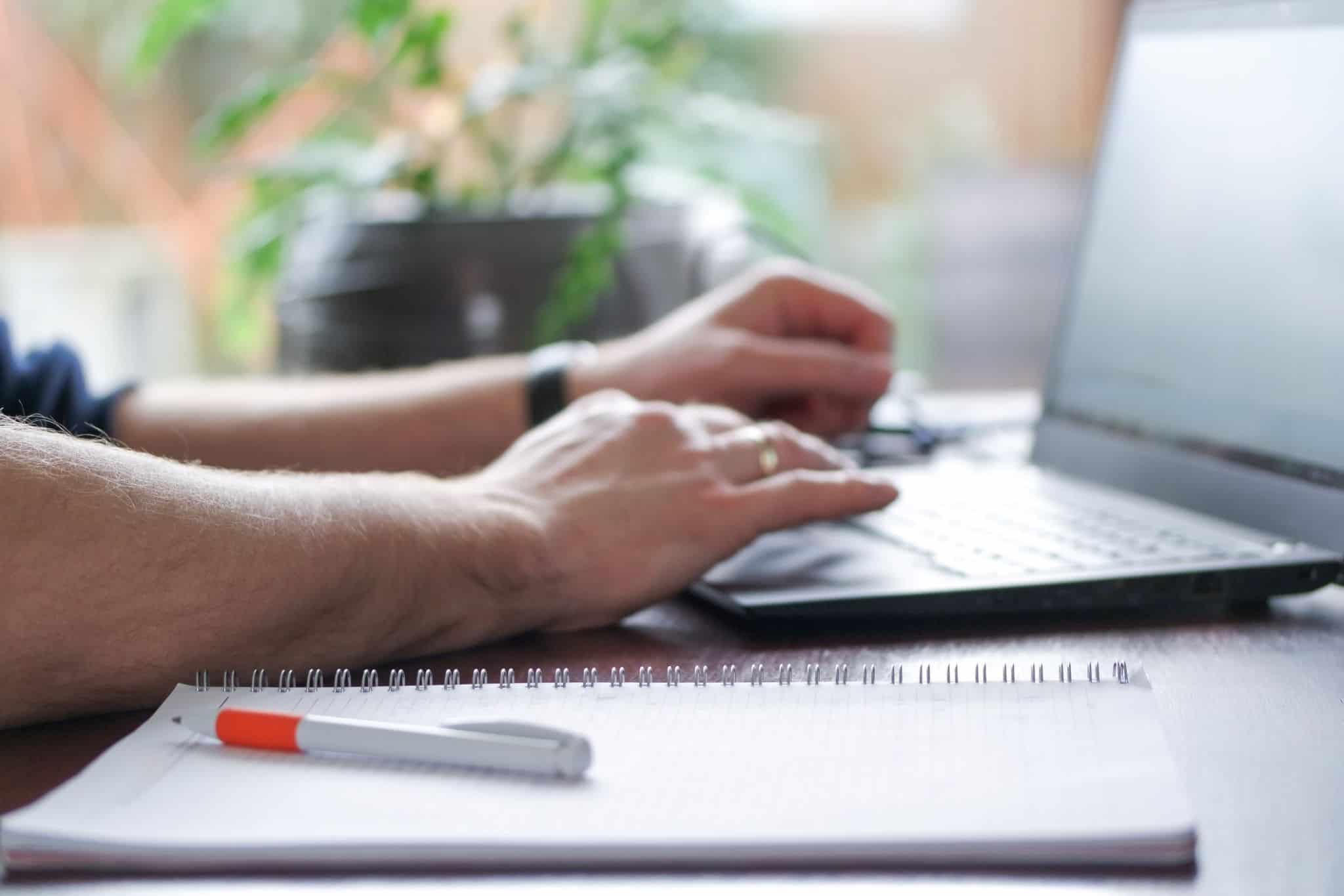 Homem ao computador com um caerno com as componentes de salário