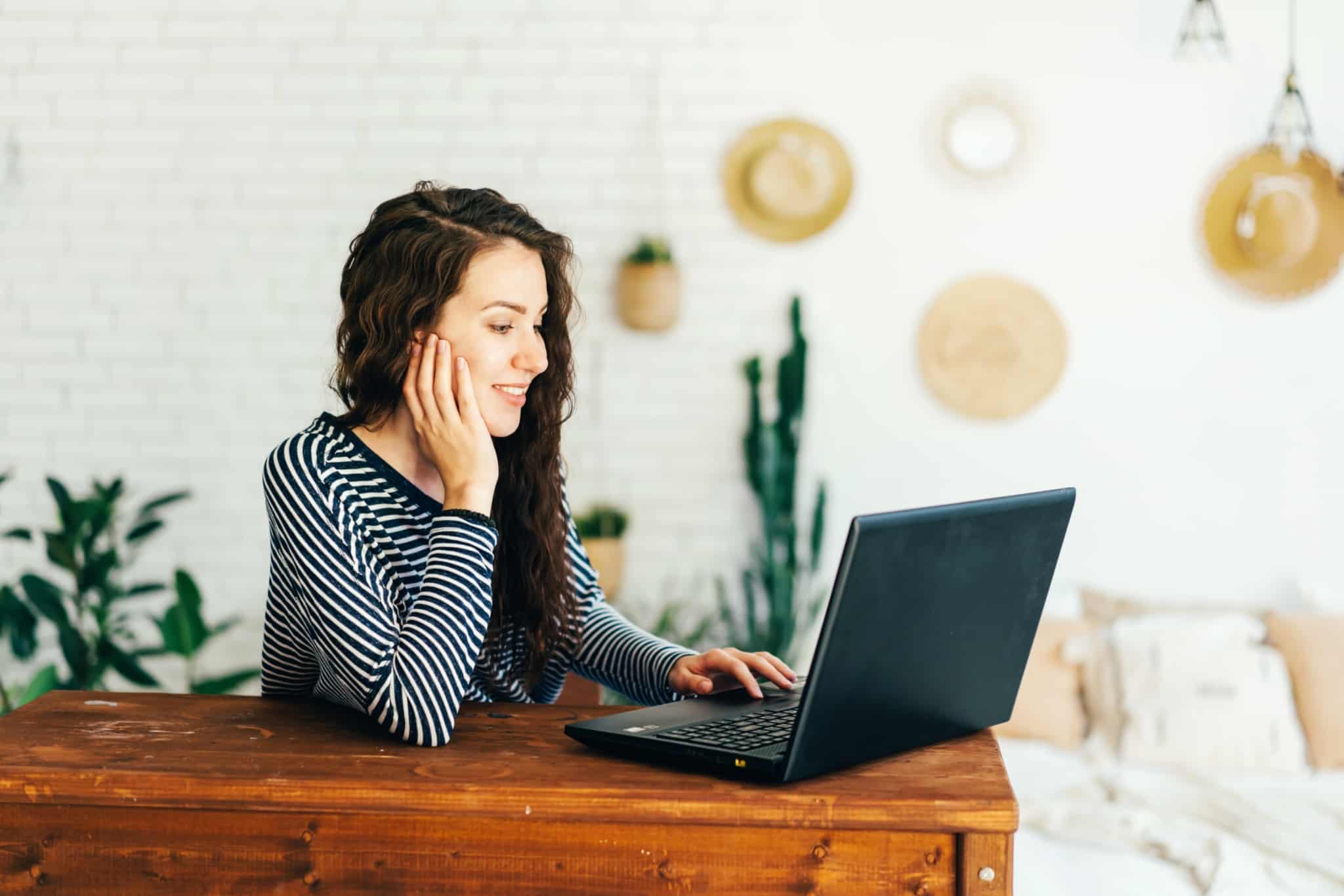 jovem mulher sentada à mesa, ao computador, num escritório em casa, em ambiente acolhedor, prepara a entrada no mercado de trabalho
