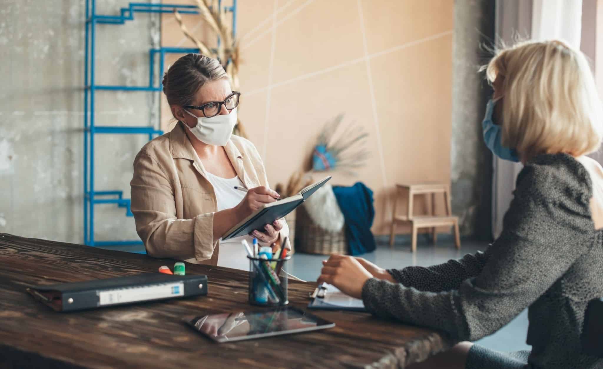 Duas mulheres de máscara a ter reunião sobre linha de apoio â empresa