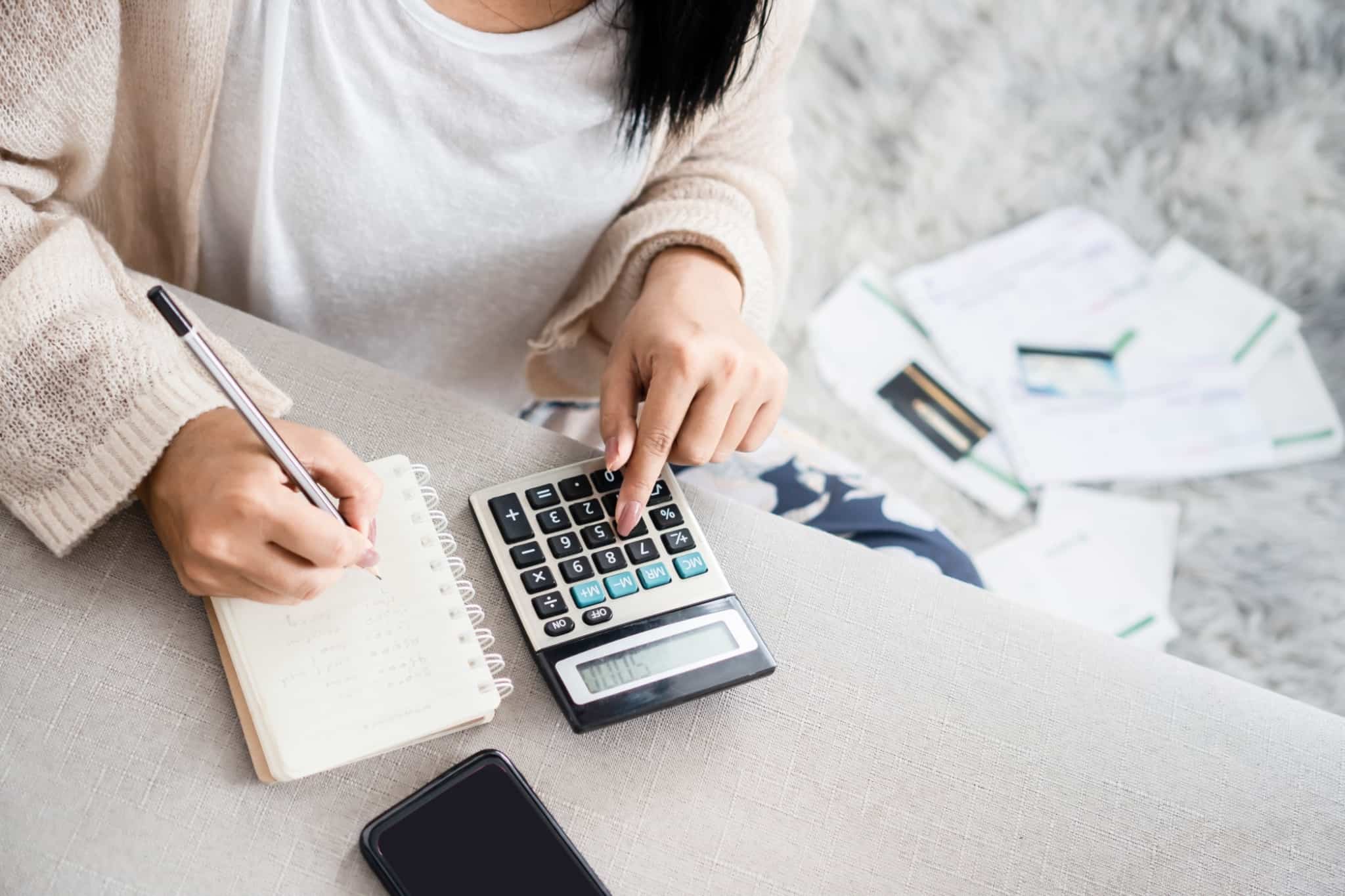 Imagem de uma mulher a fazer contas numa calculadora e com um bloco de notas - papéis, crédito, incumprimento