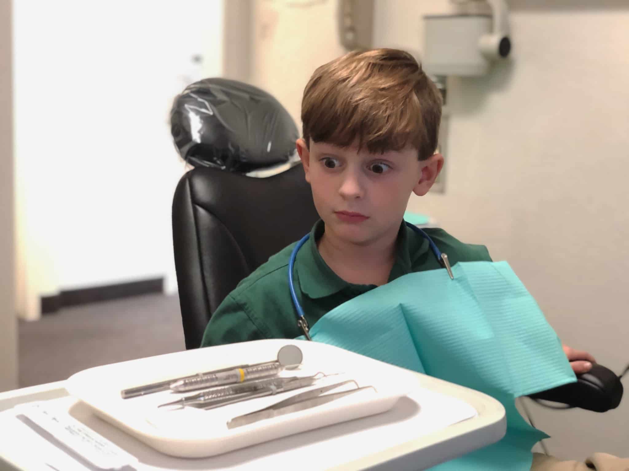 menino em consulta no dentista, já preparado, olha estupefacto e cheio de medo para os utensílios que vão ser usados pelo médico