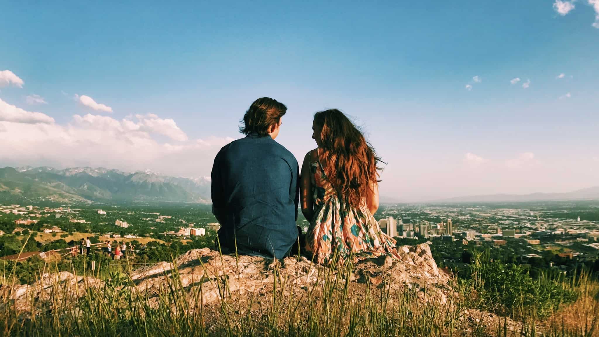 jovem casal, sentados no cume de uma serra, contemplam o horizonte
