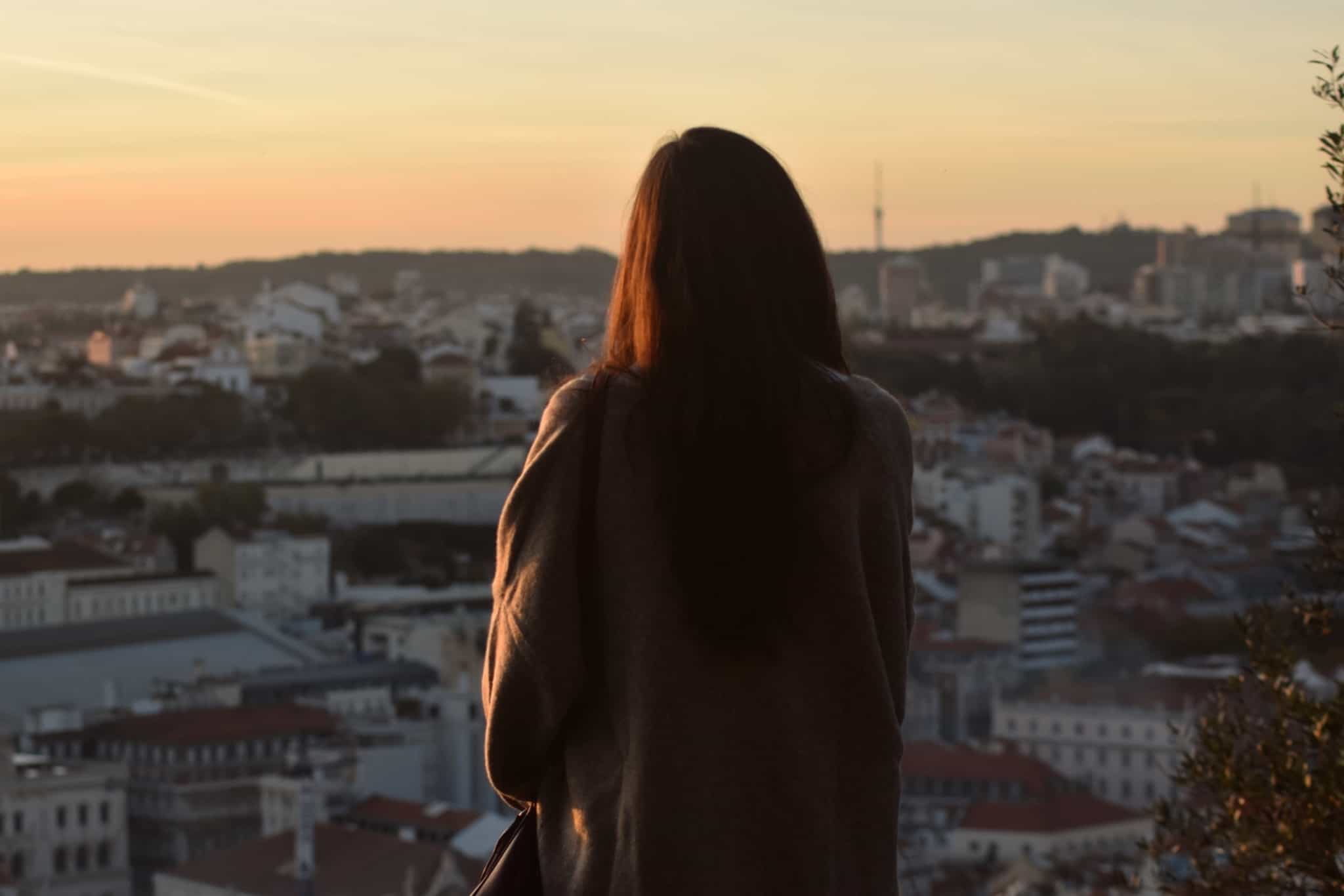 jovem mulher contempla a vista e o imenso casariono topo de uma das colinas de Lisboa