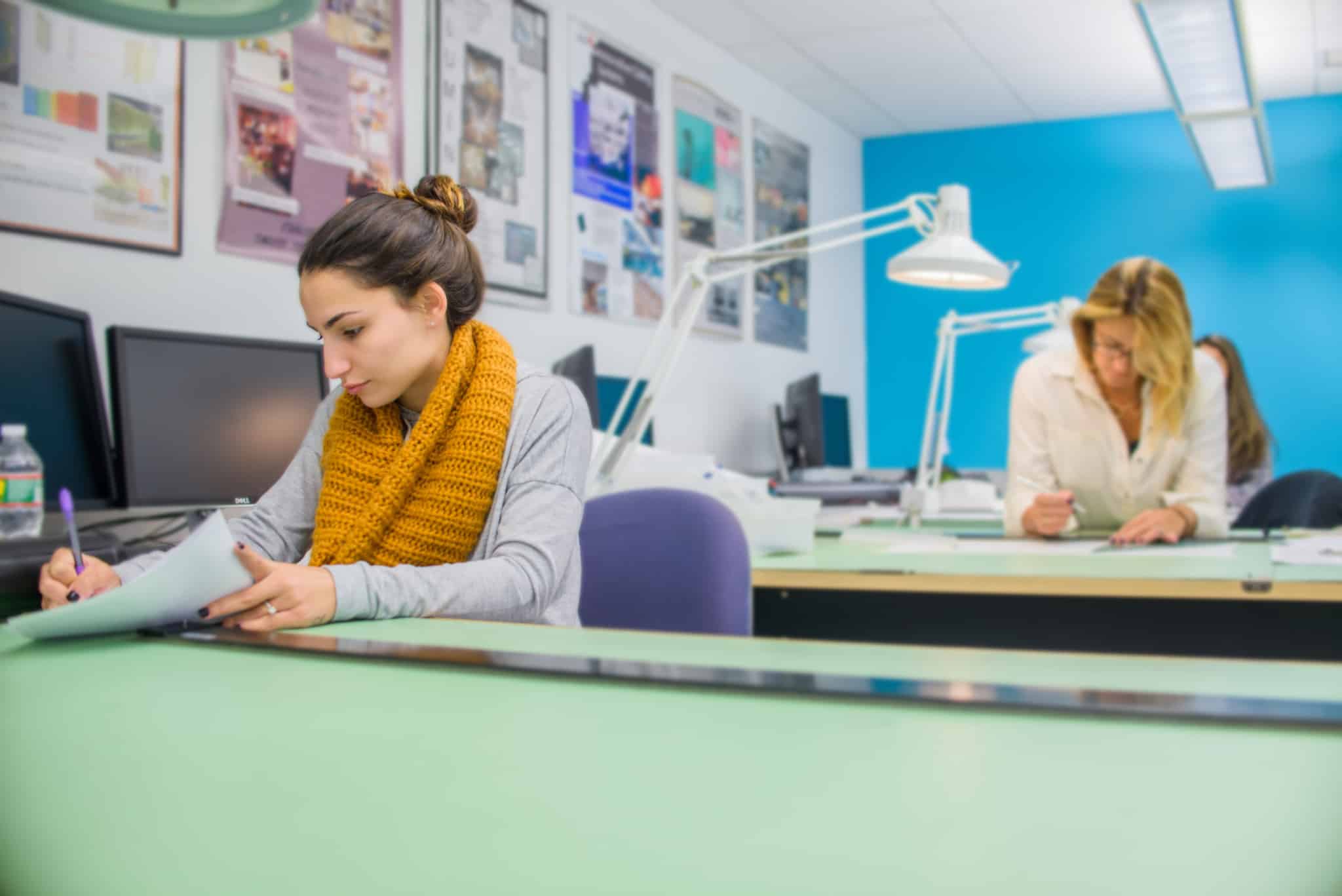 duas mulheres sentadas a trabalhar em mesas separadas no estágio a ilustrar como funciona o estágio profissional e desconto para IRS em 2023