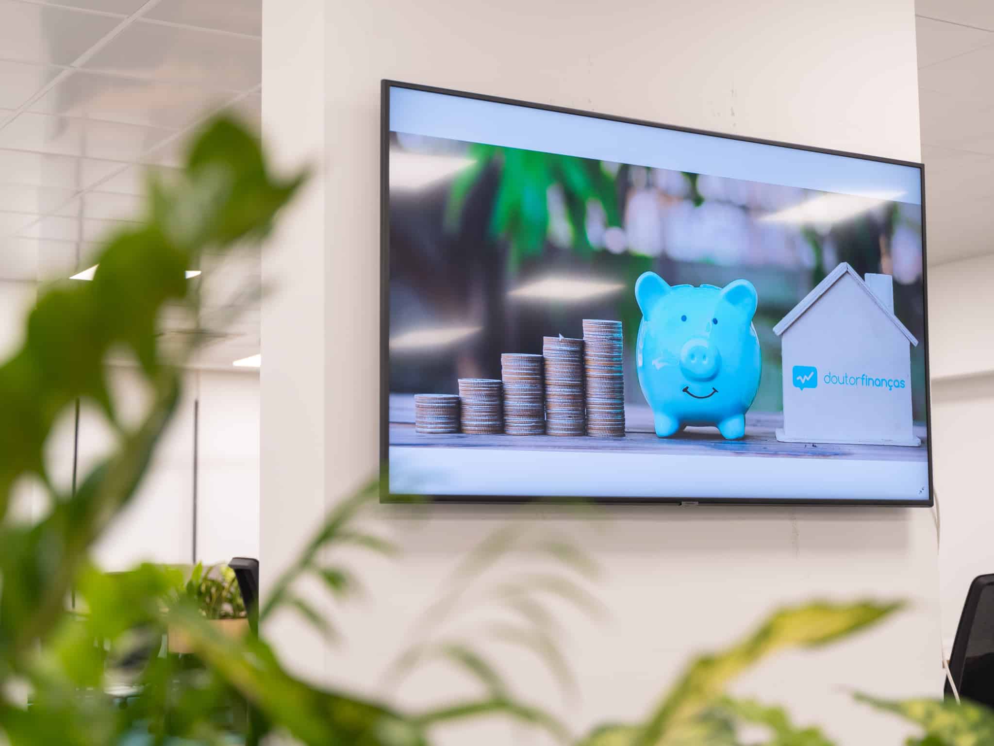 Televisor com a imagem de vários montes de moedas, um porquinho mealheiro e uma casa de madeira em miniatura. Quanto é preciso para avançar com um crédito habitação?