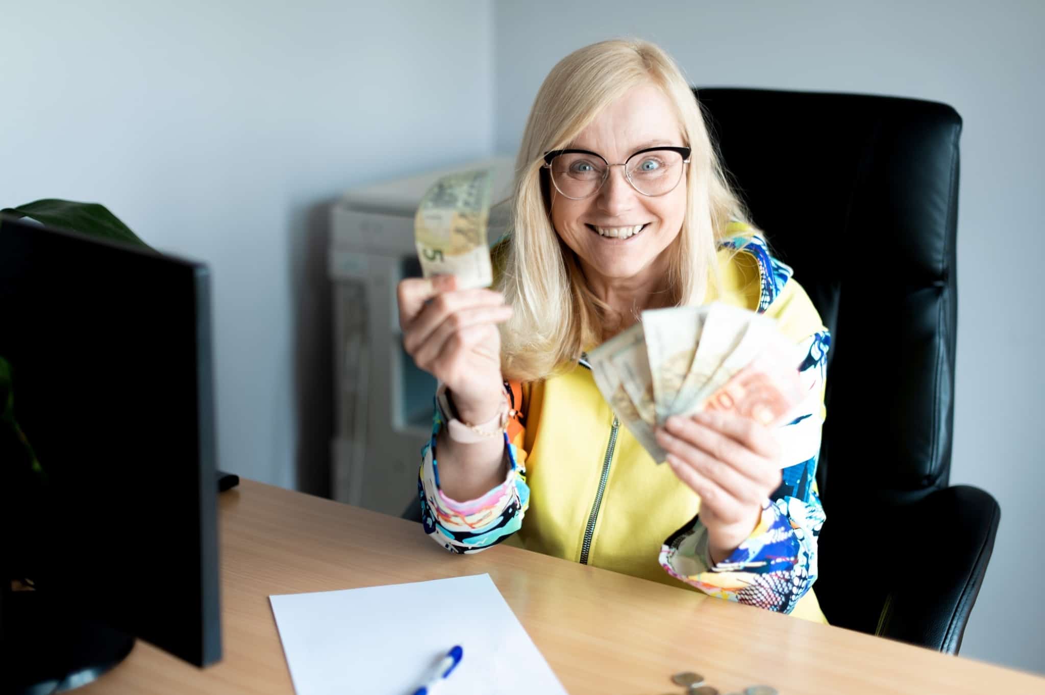 contente por não gastar dinheiro, mulher, muito sorridente, mostra uma nota de 5 euros numa mão, na outra mais notas de 10 e 20 euros