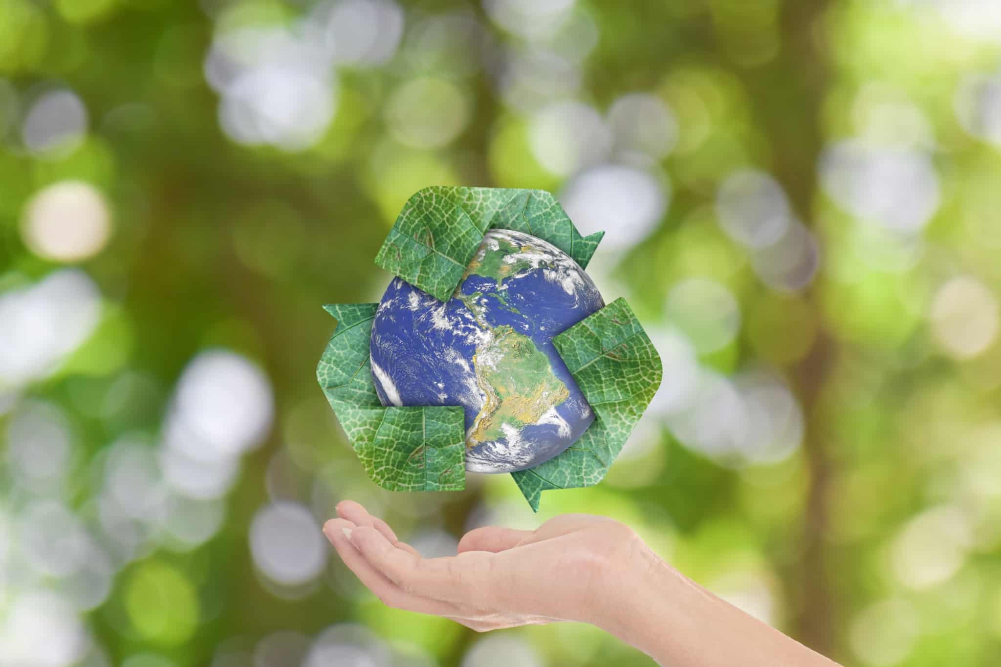 o mundo com o símbolo da reciclagem verde à volta e uma mão por baixo como se o fosse segurar