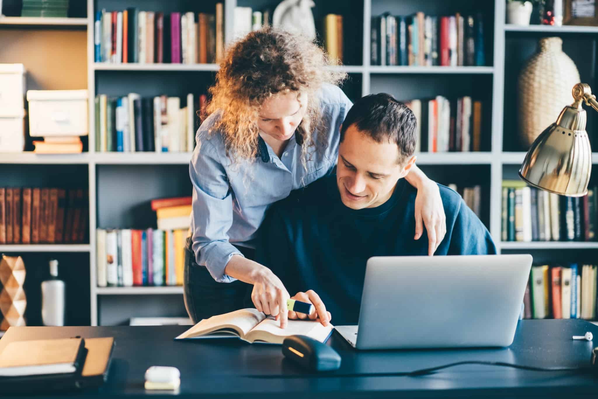 jovem casal ao computador e a consultar um livro para fazer o cálculo da atualização das rendas