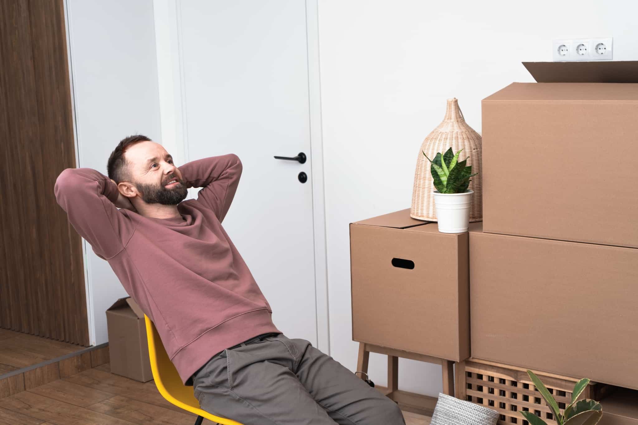 jovem rapaz, sentado numa cadeira amarela, por entre uma série de caixas de mudanças, a celebrar a compra de casa concretizada depois de alguns passos importantes