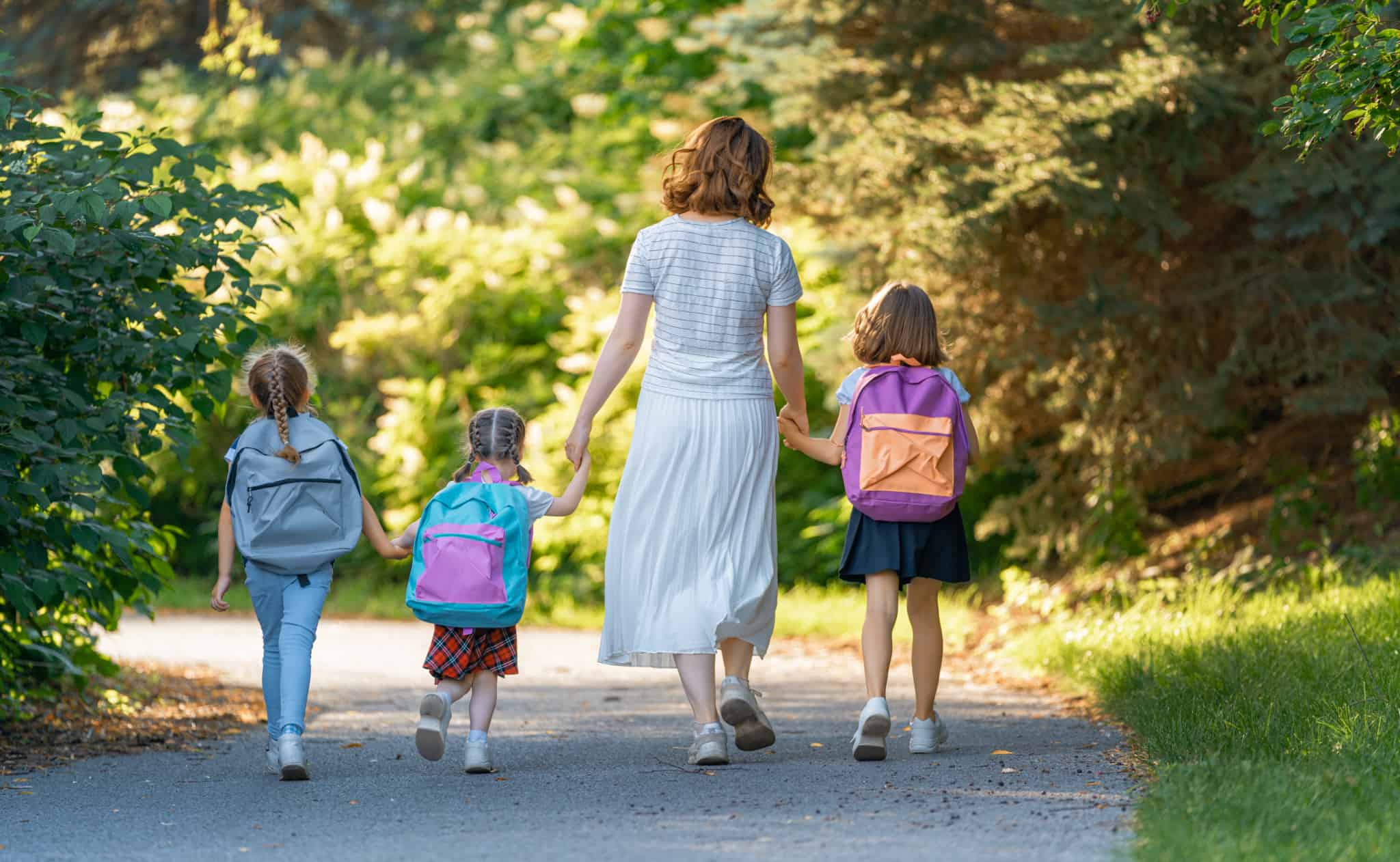 Mãe a caminhar com três filhas de costas com mochilas simbolizando primeiro ciclo