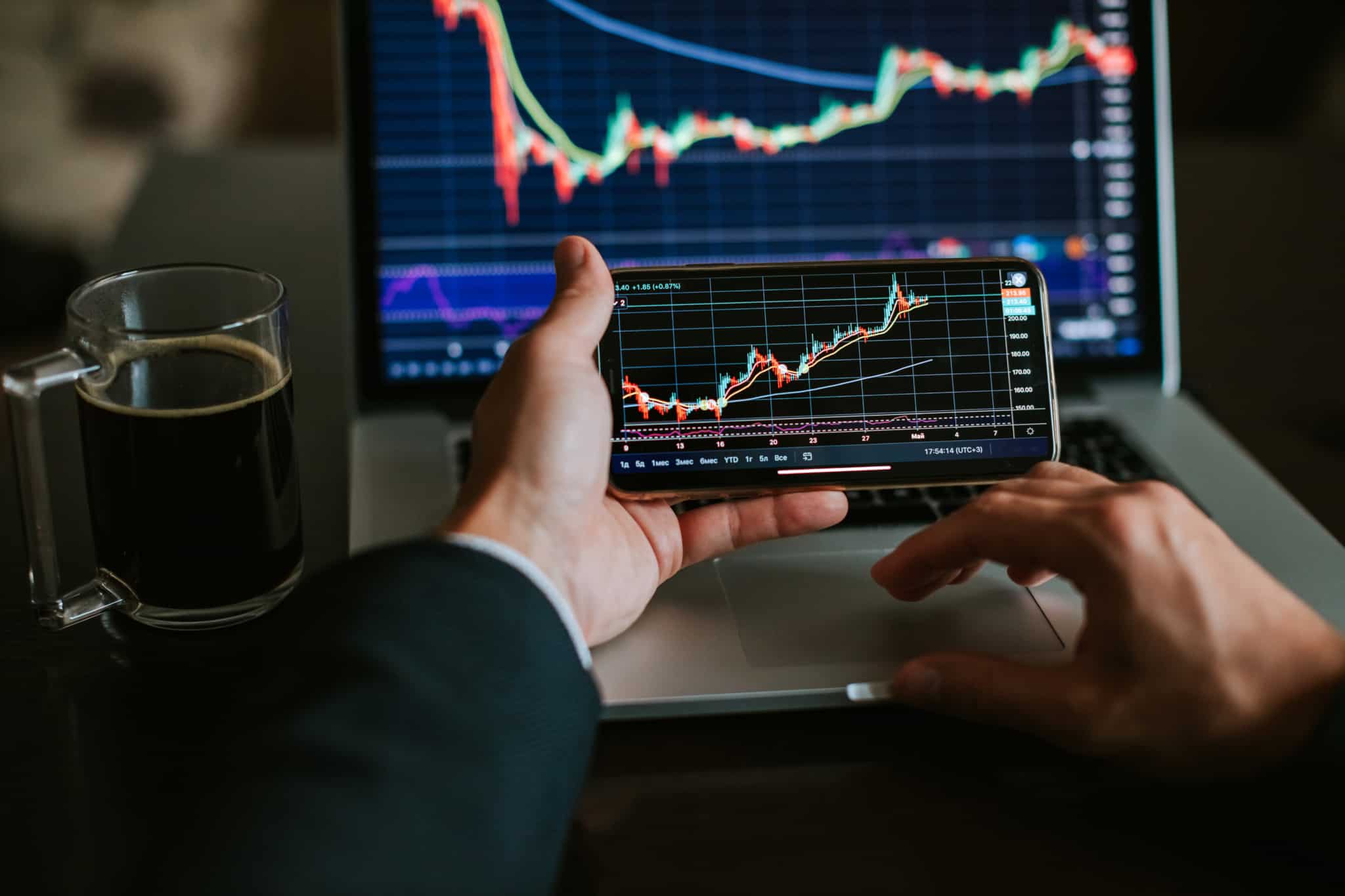 Investidor a analisar a evolução dos mercados financeiros no computador e smartphone