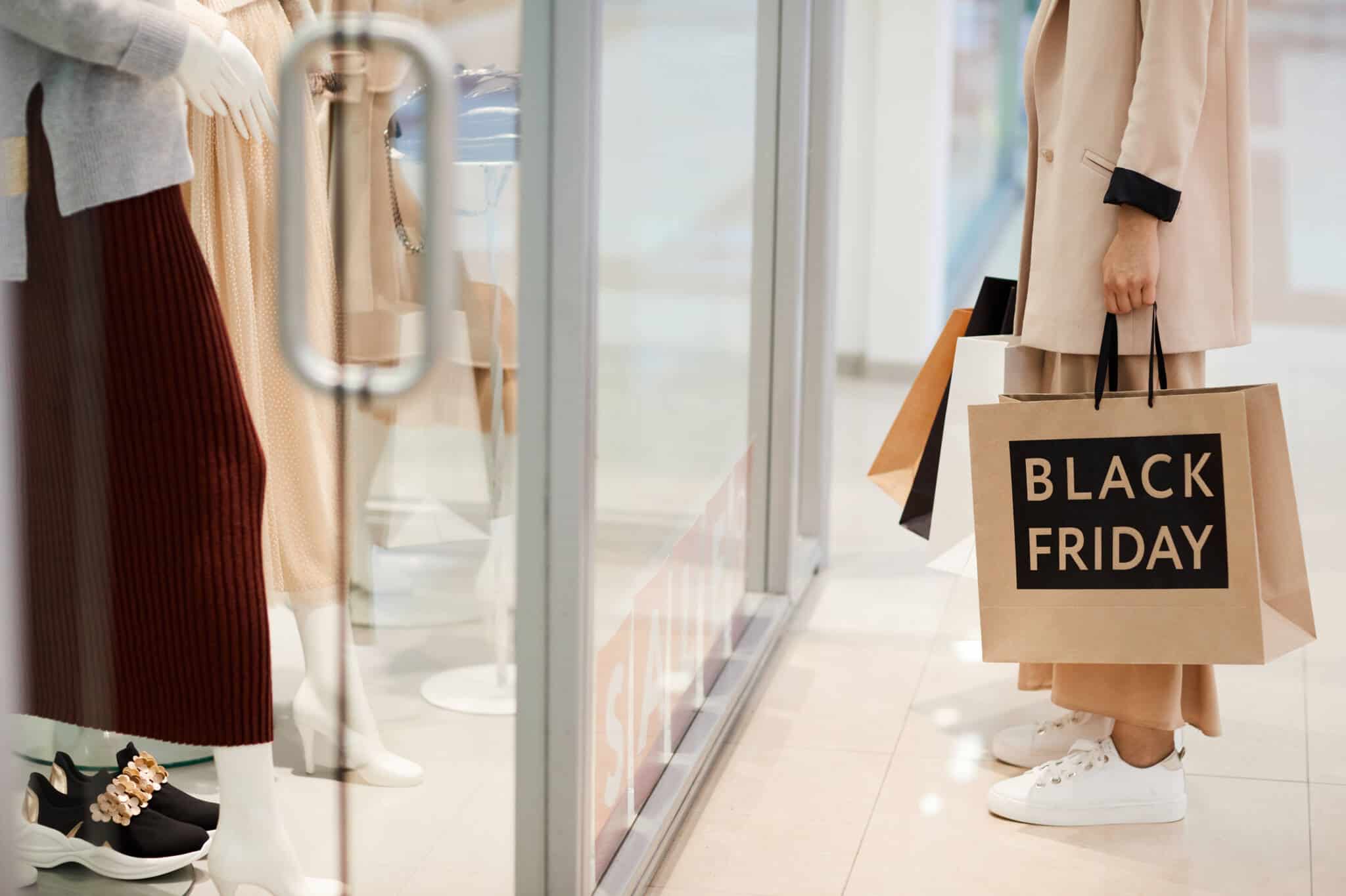Corpo de mulher a olhar para uma montra e segurar um saco que diz Black Friday