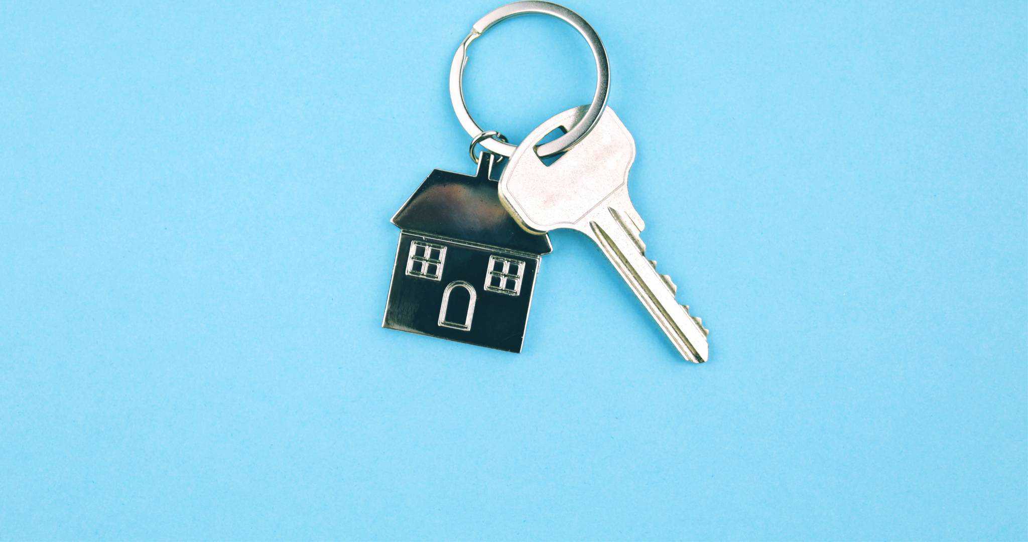Fundo azul com porta chaves com chave e pendente de casa simbolizando estrangeiro comprar casa
