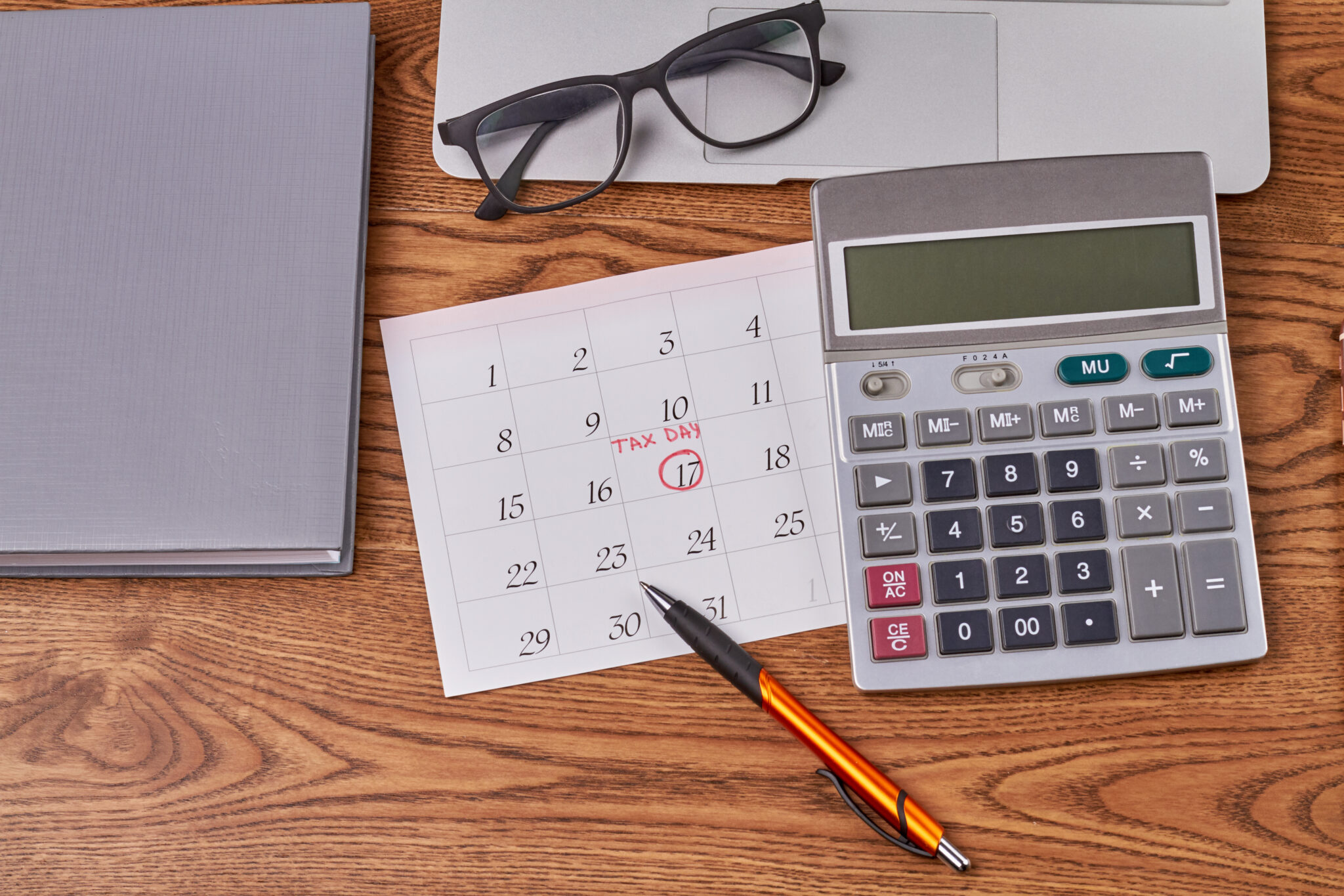 Portátil com calendário, óculos e calculadora em cima de mesa para simbolizar contas de deduções IRS