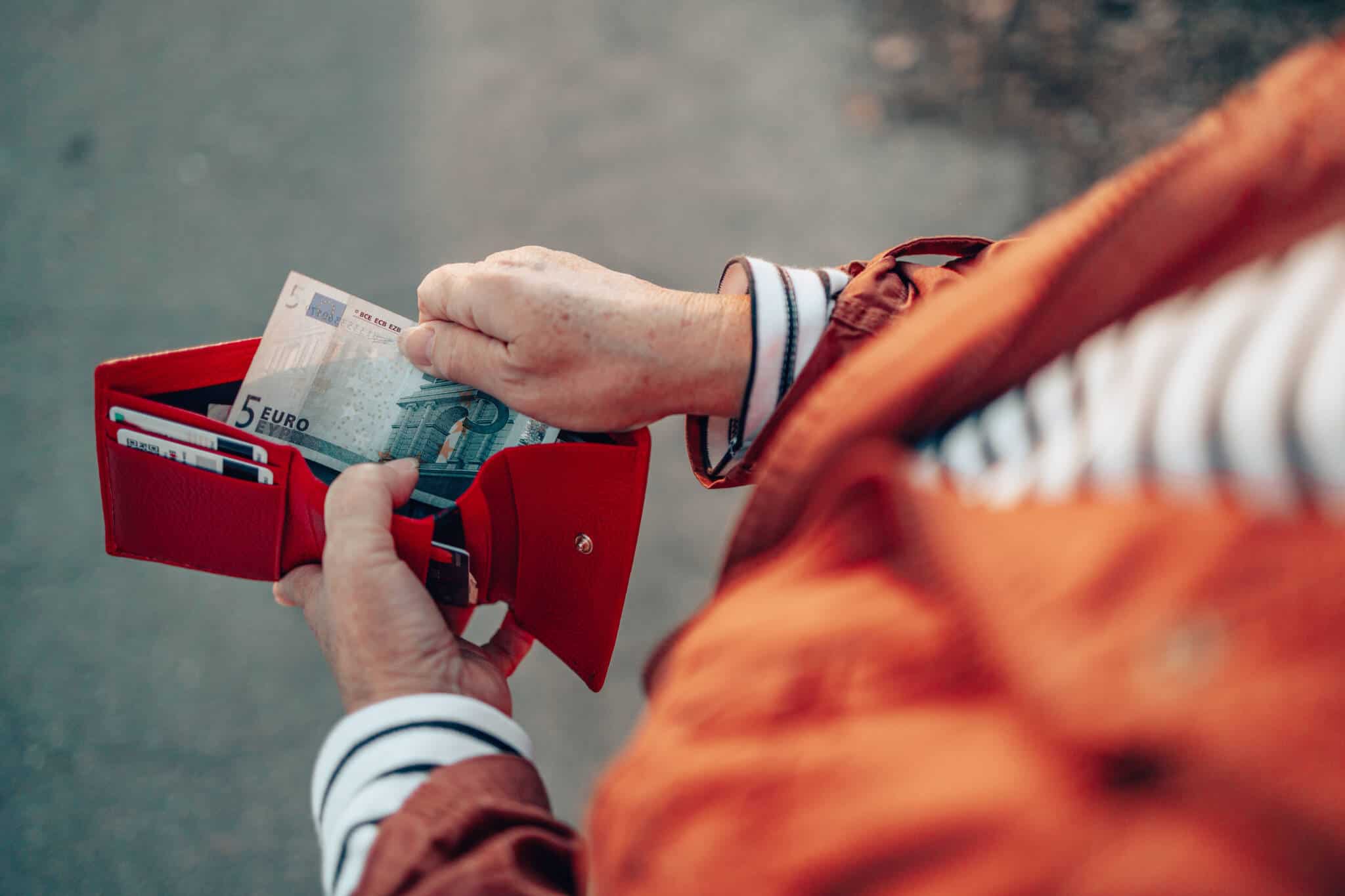 mãos de mulher (de camisola às riscas e casaco laranja) a abrir uma carteira e a retirar uma nota de 5 euros, ilustrando a redução salarial de que foi alvo