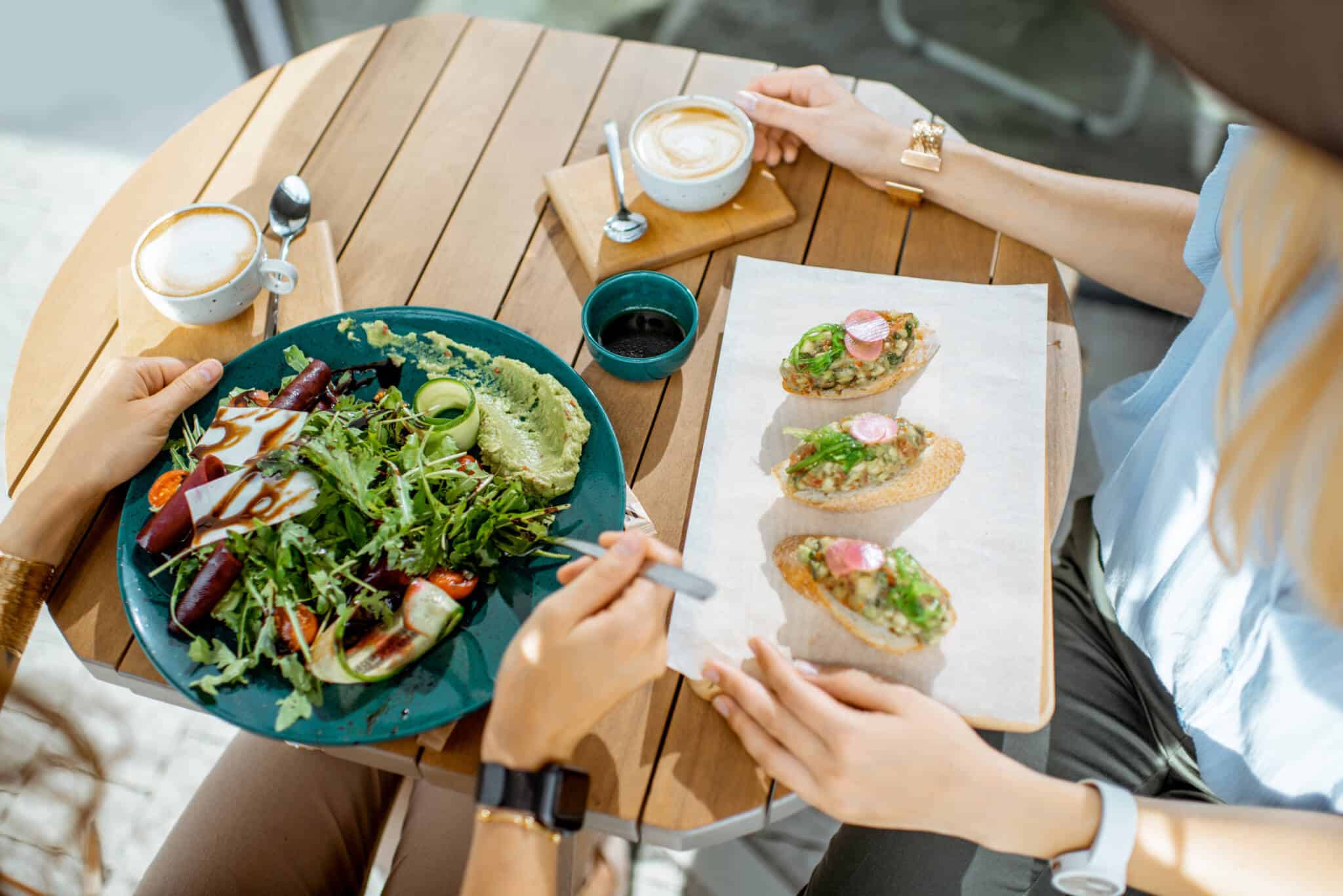 mãos de jovem casal a comer refeições saudáveis, verdes e fescas, sentados à mesa de um restaurante, fazendo assim uma alimentação saudável