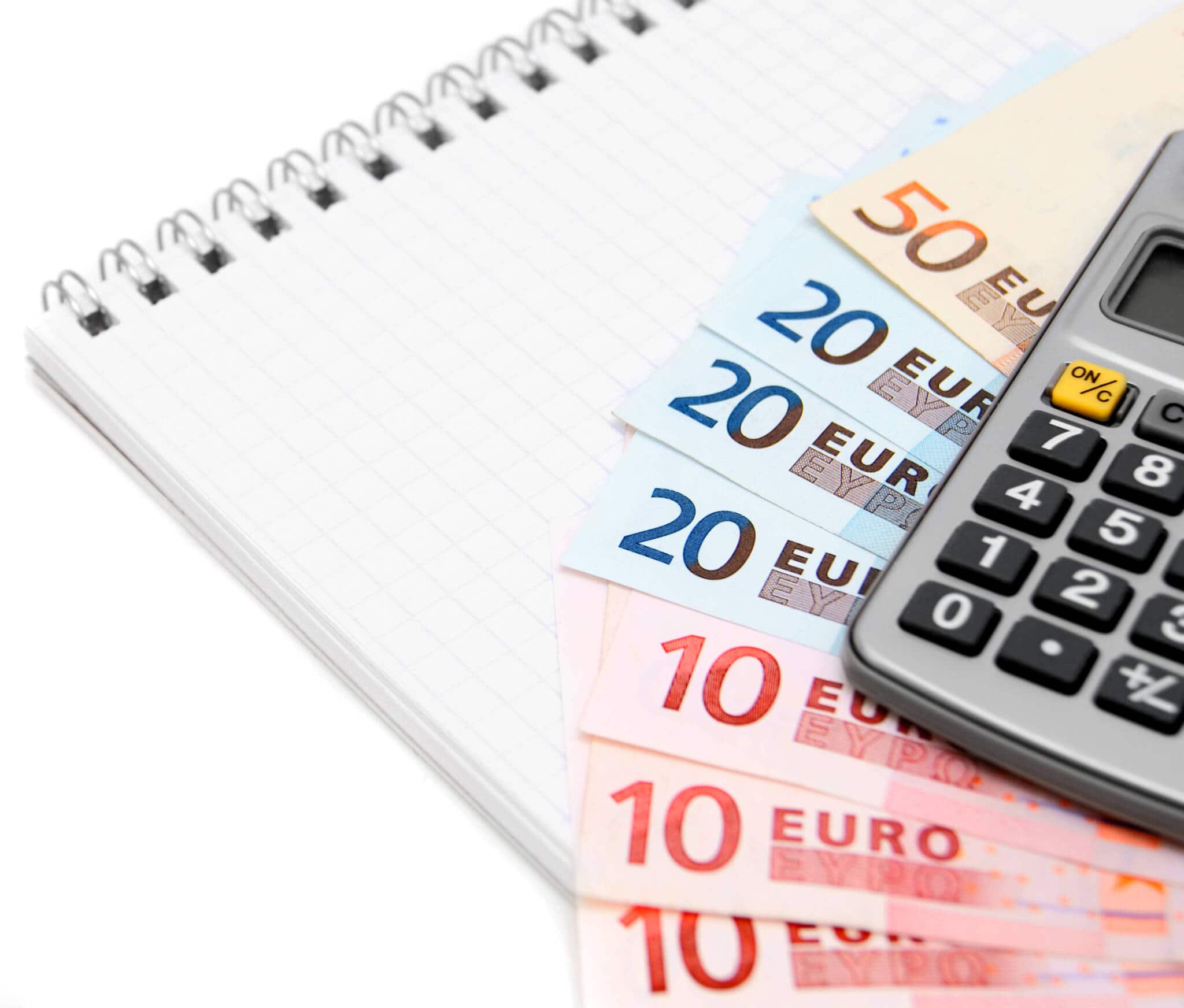 Uma série de notas de euro (50, 20 e 10 euros) colocadas em cima de um bloco de notas em formato leque. Por cima está uma calculadora, numa alusão à contabilidade