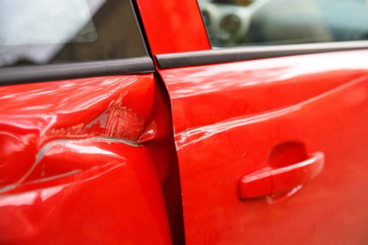 Carro vermelho com a porta estragada depois de um acidente