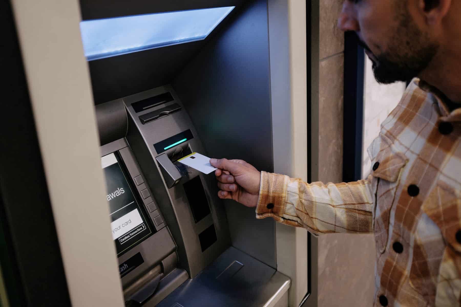 Como ver débitos diretos no multibanco? homem a inserir cartão na caixa ATM para ver débitos diretos no multibanco